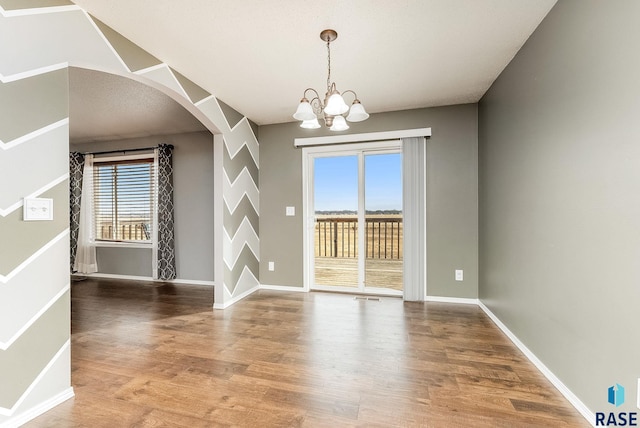 unfurnished dining area featuring arched walkways, baseboards, and wood finished floors