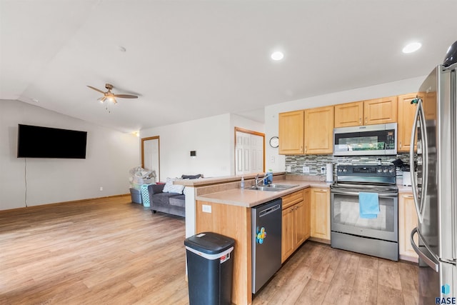 kitchen featuring open floor plan, a peninsula, stainless steel appliances, light wood-style floors, and a sink