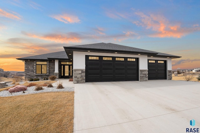 prairie-style house with a garage, stone siding, concrete driveway, and stucco siding