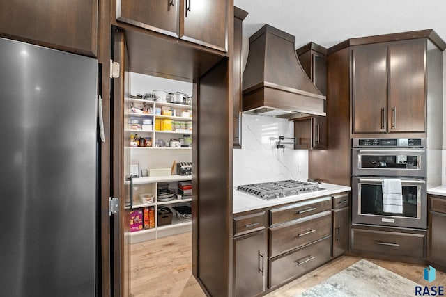 8501 E Torchwood Pl, Sioux Falls, SD 57110 - kitchen with dark brown cabinetry, custom exhaust hood, stainless steel appliances, light countertops, and light wood-type flooring