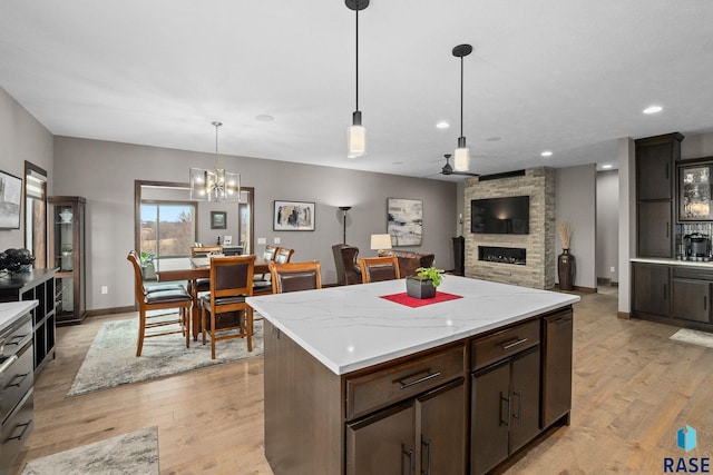 8501 E Torchwood Pl, Sioux Falls, SD 57110 - kitchen with dark brown cabinetry, a kitchen island, hanging light fixtures, light wood-style floors, and a fireplace