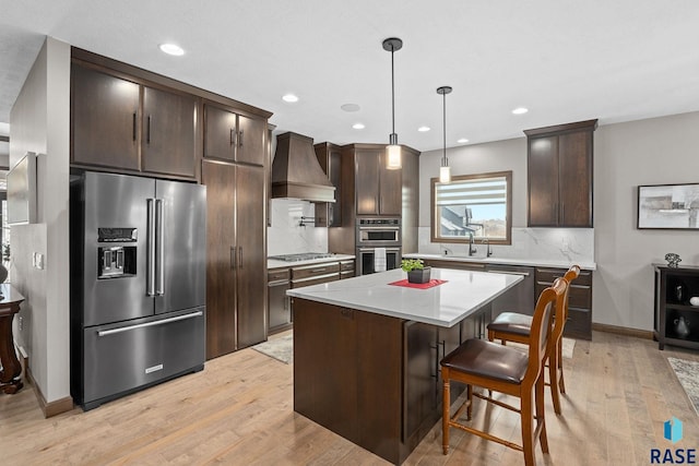 kitchen with light wood-style flooring, appliances with stainless steel finishes, dark brown cabinets, premium range hood, and a sink