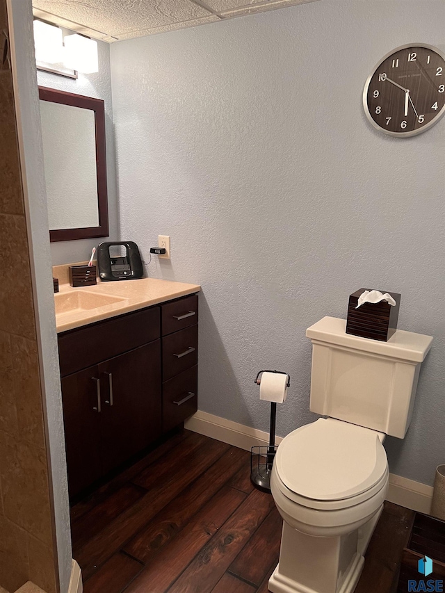 half bathroom with a textured wall, toilet, vanity, wood finished floors, and baseboards