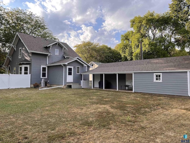 back of house with a yard, fence, and a shingled roof