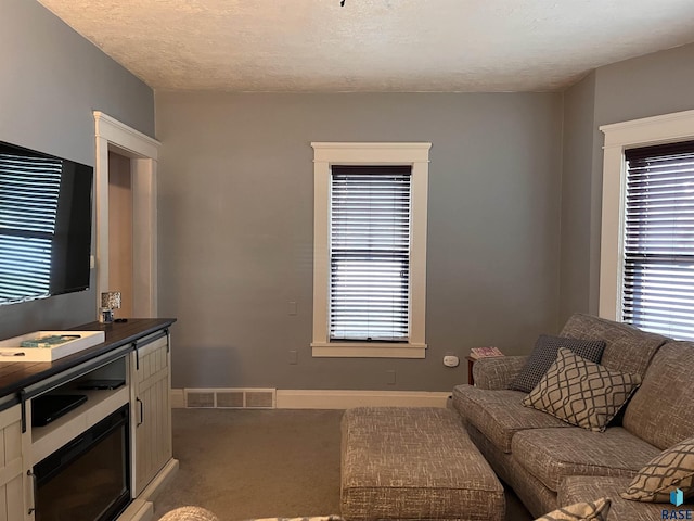 carpeted living room featuring baseboards, visible vents, and a textured ceiling