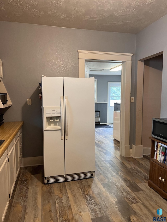 kitchen with a textured ceiling, white refrigerator with ice dispenser, dark wood finished floors, and baseboards