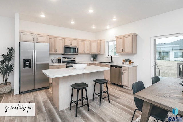 kitchen featuring appliances with stainless steel finishes, a center island, light countertops, light brown cabinetry, and a sink