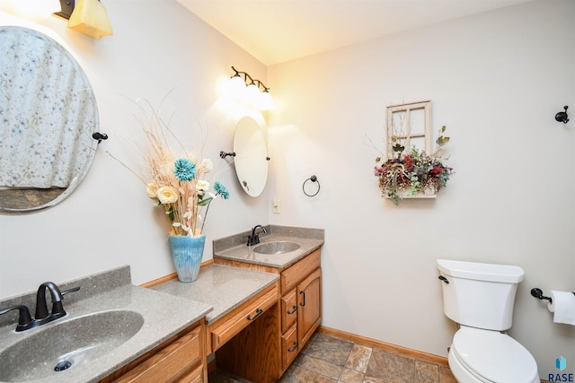 full bathroom featuring toilet, double vanity, baseboards, and a sink