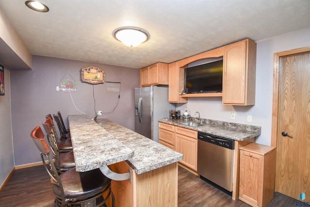 kitchen featuring stainless steel appliances, dark wood finished floors, a sink, and a kitchen breakfast bar