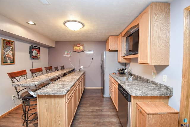 kitchen with light brown cabinets, a peninsula, a sink, stainless steel dishwasher, and a kitchen bar