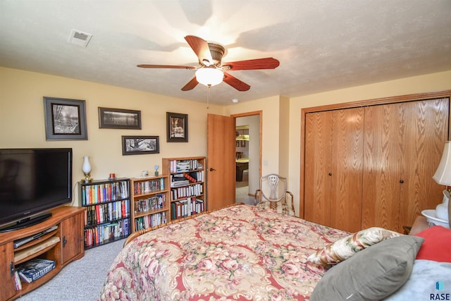 carpeted bedroom with a textured ceiling, ceiling fan, a closet, and visible vents