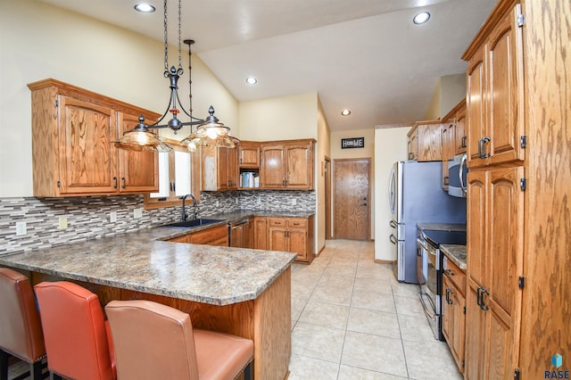 kitchen featuring brown cabinetry, appliances with stainless steel finishes, a peninsula, a sink, and light tile patterned flooring