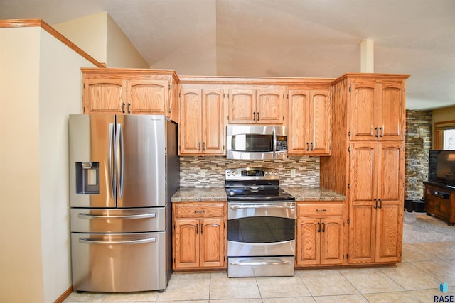 kitchen featuring brown cabinets, light tile patterned floors, stainless steel appliances, tasteful backsplash, and stone countertops