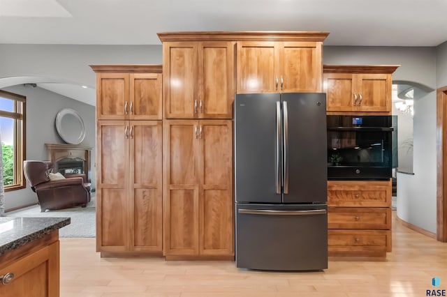 kitchen featuring freestanding refrigerator, oven, arched walkways, and dark stone countertops