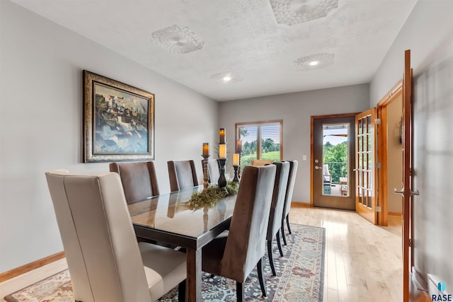 dining area featuring a textured ceiling, light wood-type flooring, and baseboards