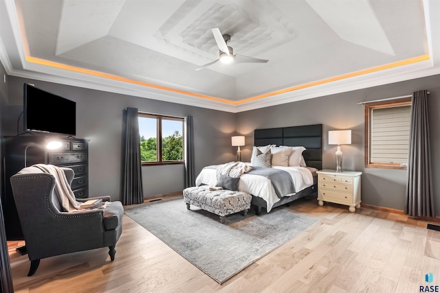 bedroom featuring light wood-style flooring, a raised ceiling, and a ceiling fan