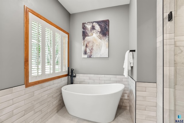 full bath featuring a soaking tub, tile walls, and wainscoting