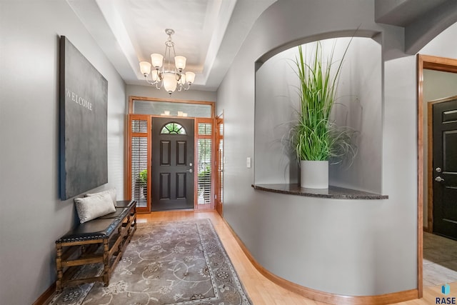 entryway with a chandelier, a raised ceiling, wood finished floors, and baseboards