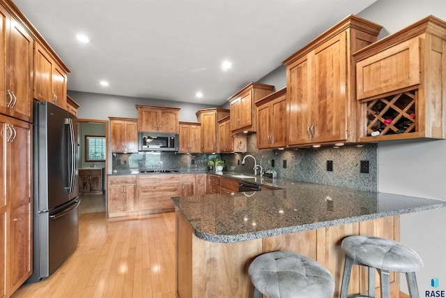 kitchen featuring a peninsula, a sink, appliances with stainless steel finishes, backsplash, and dark stone countertops