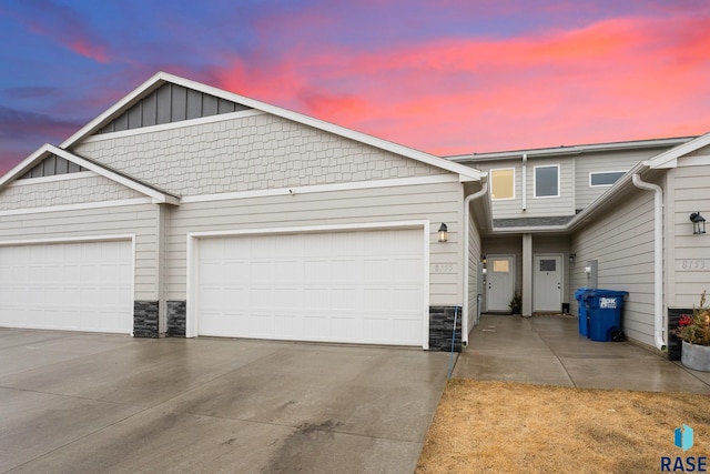 townhome / multi-family property featuring a garage, stone siding, board and batten siding, and driveway