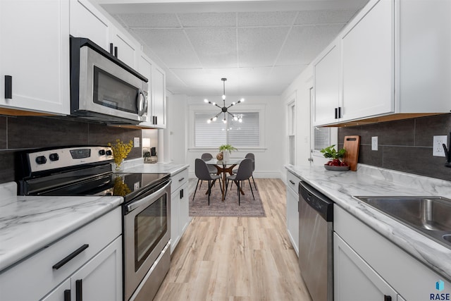 kitchen with tasteful backsplash, appliances with stainless steel finishes, light wood-style flooring, and white cabinets