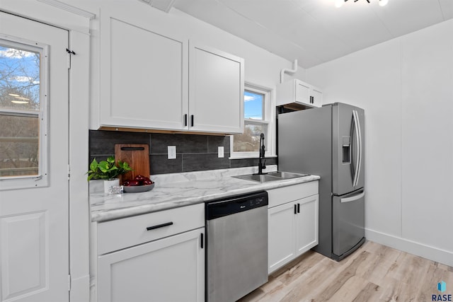 kitchen featuring a sink, stainless steel appliances, light wood-style floors, white cabinetry, and backsplash