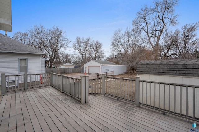 wooden terrace featuring a detached garage, fence, and an outbuilding