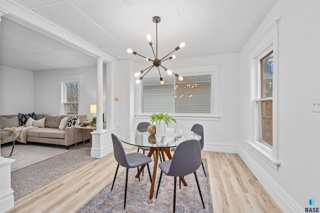 dining area featuring ornate columns, baseboards, light wood finished floors, and an inviting chandelier