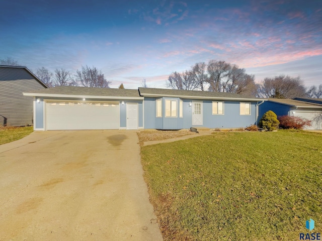 ranch-style house featuring a garage, concrete driveway, and a yard