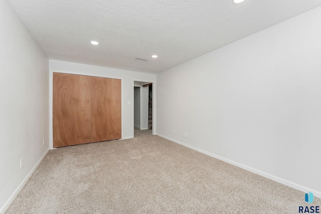 unfurnished bedroom with a textured ceiling, a closet, baseboards, and light colored carpet