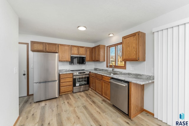 kitchen with stainless steel appliances, light wood-type flooring, a sink, and brown cabinets