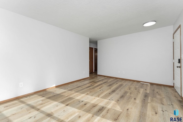 spare room featuring a textured ceiling, light wood finished floors, and baseboards