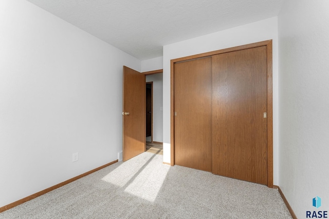 unfurnished bedroom featuring carpet floors, a textured ceiling, baseboards, and a closet