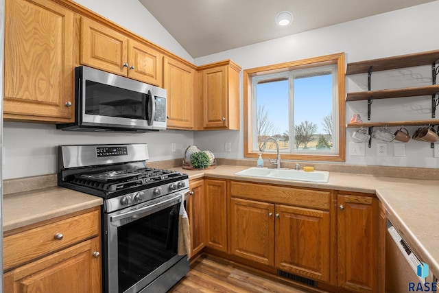 kitchen featuring light wood-style flooring, stainless steel appliances, a sink, vaulted ceiling, and light countertops