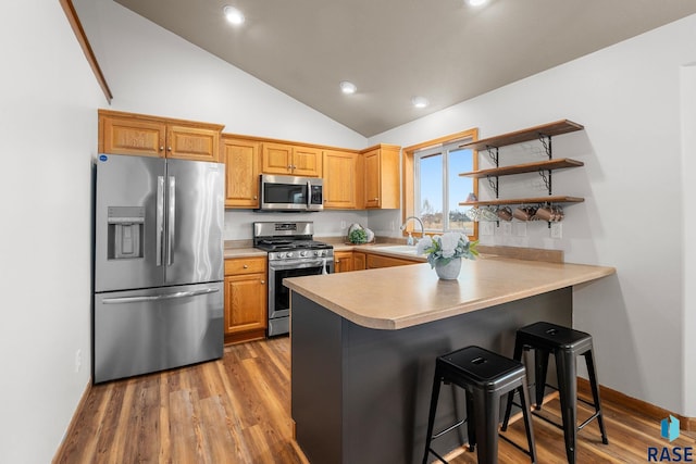 kitchen featuring a peninsula, wood finished floors, light countertops, appliances with stainless steel finishes, and a kitchen bar