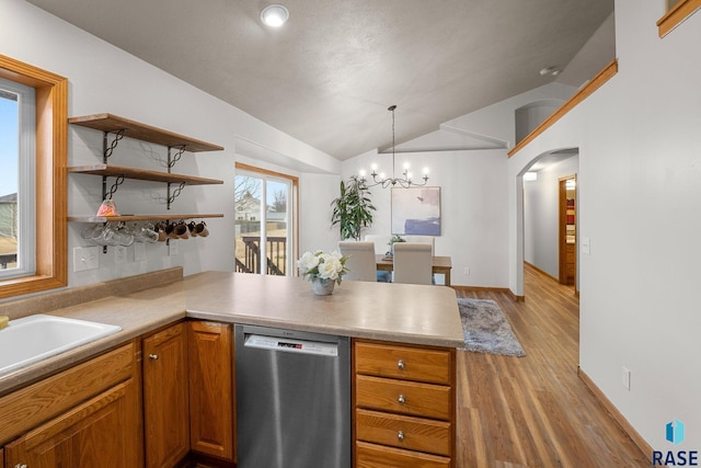 kitchen featuring arched walkways, a peninsula, vaulted ceiling, stainless steel dishwasher, and light wood-type flooring