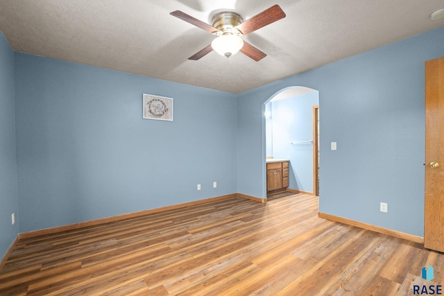 empty room with arched walkways, baseboards, ceiling fan, and light wood finished floors