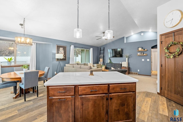 kitchen with light wood-type flooring, vaulted ceiling, hanging light fixtures, and open floor plan