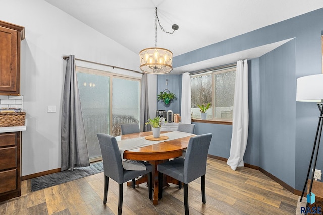 dining room featuring lofted ceiling, light wood-type flooring, a chandelier, and baseboards