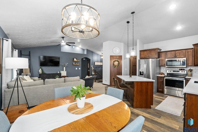 dining space featuring arched walkways, dark wood-type flooring, ceiling fan with notable chandelier, vaulted ceiling, and recessed lighting