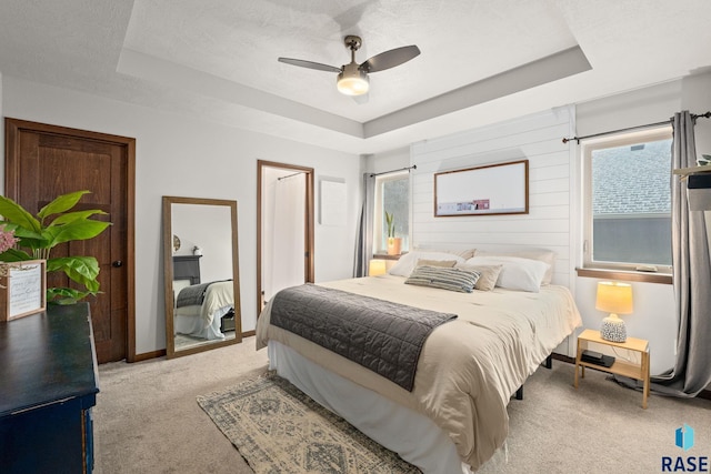 carpeted bedroom with a textured ceiling, ceiling fan, and a raised ceiling