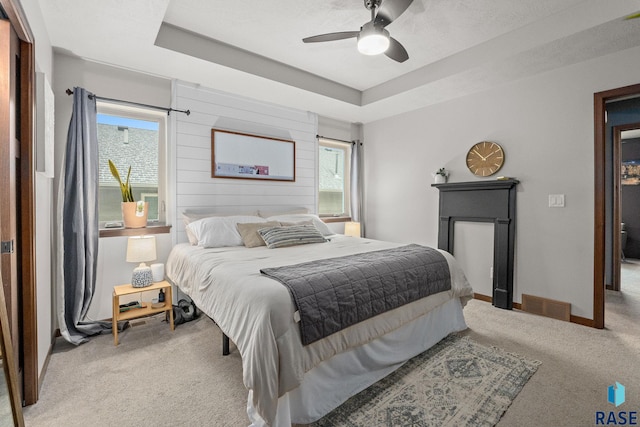 bedroom featuring light colored carpet, a raised ceiling, visible vents, and baseboards