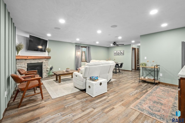 living area featuring light wood finished floors, baseboards, ceiling fan, a stone fireplace, and recessed lighting