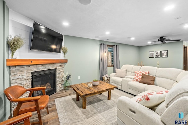 living area with recessed lighting, a ceiling fan, wood finished floors, and a stone fireplace