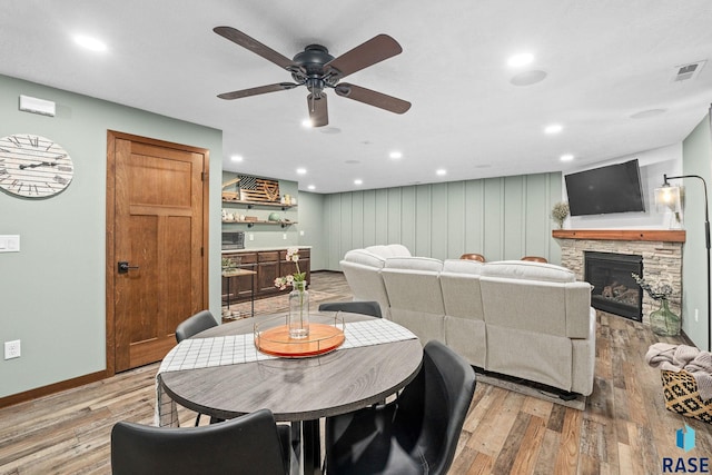 dining area featuring light wood-style flooring, visible vents, a stone fireplace, and baseboards