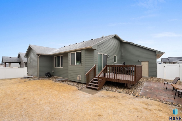 rear view of property featuring a patio, a fenced backyard, roof with shingles, a wooden deck, and a gate