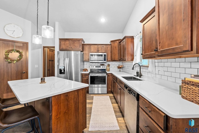 kitchen with a breakfast bar area, appliances with stainless steel finishes, a center island, vaulted ceiling, and a sink