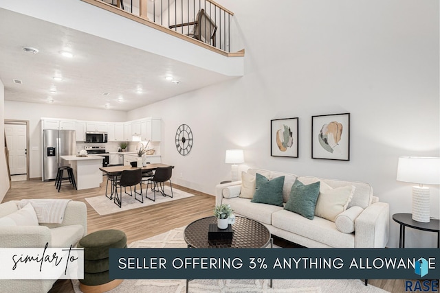 living area featuring light wood-type flooring, a towering ceiling, and baseboards