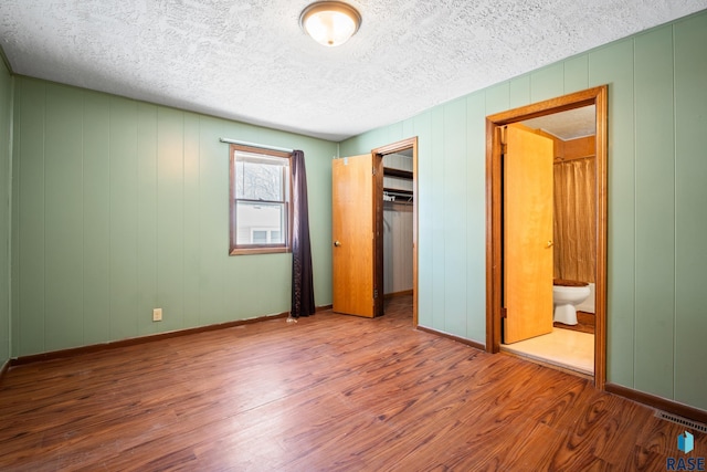 unfurnished bedroom with a textured ceiling, baseboards, and wood finished floors