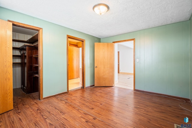 unfurnished bedroom featuring a textured ceiling, wood finished floors, baseboards, a closet, and a walk in closet